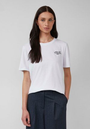T-shirt en coton blanc avec des manches courtes et un col rond, portant un texte noir brodé sur la poitrine disant "Prends ton cœur en pain d'épices."