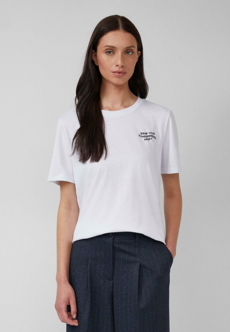 T-shirt en coton blanc avec des manches courtes et un col rond, portant un texte noir brodé sur la poitrine disant "Prends ton cœur en pain d'épices."