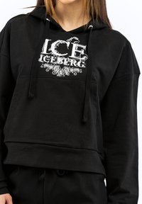 Čierna mikina s kapucňou s predným vreckom, s bielym grafickým motívom "ICE ICEBERG" a šnúrkami. Mäkkučká, textúrovaná látka, skrátený strih.