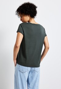 Mörkgr�ön kortärmad t-shirt med avslappnad passform, rund halsringning och mjuk textur. Bärs med ljusblå löst sittande jeans.