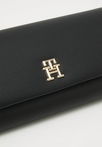 Svart lær clutch med teksturert overflate, med et gulllogo-aksent. Slank rektangulær form, brettet design.