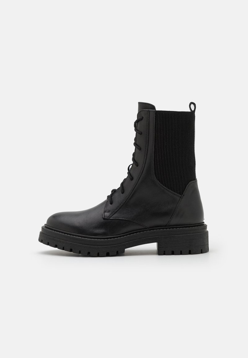Czarne skórzane buty wojskowe z wiązaniem z przodu, żeberkową dzianinową panelem wokół kostki, pętlą do zakupu oraz grubą, solidną podeszwą na białym tle.