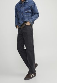 Džínová bunda v světle modré s dvěma náprsními kapsami, spárovaná s volnými šedými džíny a hnědými teniskami s bílými pruhy.