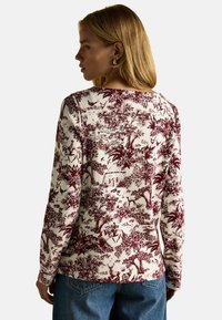 Dlhý rukáv z bavlny v off-whites farbe s burgundským podrobným krajinným tlačom, ktorý zobrazuje stromy, postavy a architektúru.