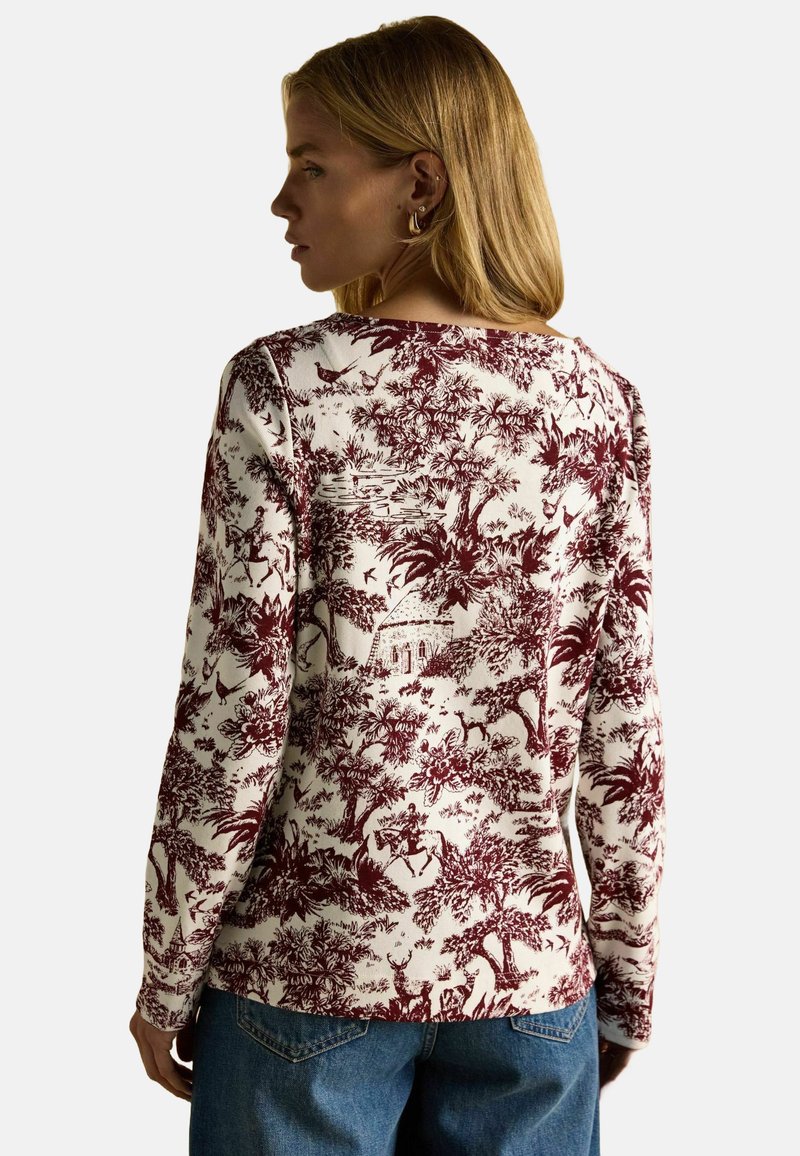 Dlhý rukáv z bavlny v off-whites farbe s burgundským podrobným krajinným tlačom, ktorý zobrazuje stromy, postavy a architektúru.