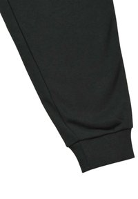 Pantalones deportivos negros con una textura suave, que cuentan con puños elásticos y un diseño ajustado. Construcción simple sin marcas ni patrones visibles.
