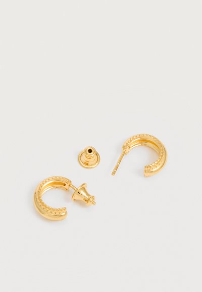 Pereche de cercei mici rotunzi din aur cu un design texturat, unul cu sistemul de prindere îndepărtat, așezați pe o suprafață neutră și deschisă la culoare.