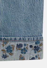 Denim bleu clair avec une broderie florale dans des nuances de bleu et de marron à l'ourlet, avec un bord effiloché et une texture subtile.