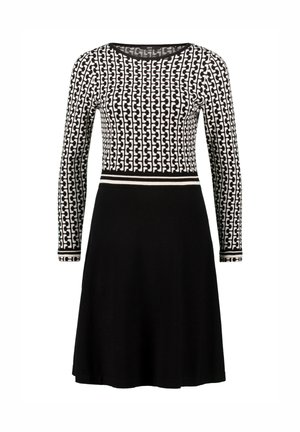 Langarm jurk met een zwart-witte geometrische patroon top en een effen zwarte rok, met een contrasterende tailleband detail.