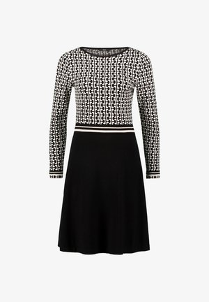 Langärmliges Kleid mit einem schwarz-weißen geometrischen Muster im Oberteil und einem einfarbigen schwarzen Rock, versehen mit einem kontrastierenden Taillendetail.