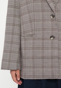 Bruin en wit geblokte blazer met een revers, twee knopen en zijzakken; gestructureerde vorm en textiele stof met een getailleerde pasvorm.