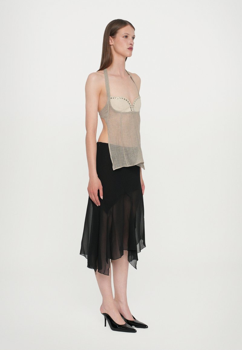 Sheer beige top with decorative stitching and cutouts, paired with a black, layered flared skirt, worn with black high-heeled shoes.