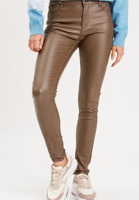 Braune Fake-Leder-Leggings mit einer figurschmeichelnden Passform, hohem Bund und glatter Oberfläche, kombiniert mit hellen Sneakers.
