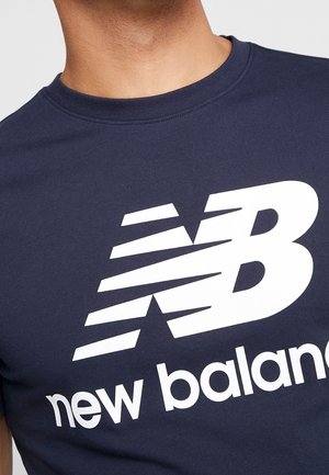 Marineblå bomulds-T-shirt med rund hals, der har en stor hvid "NB"-logo og teksten "new balance" i fed, moderne skrifttype.