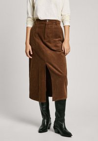 Falda midi de pana marrón con abertura frontal, con cintura alta y bolsillos, combinada con botas negras de tacón hasta la rodilla.