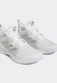 Vita atletiska skor med ett textilöverdrag, ribbad textur och tre silverstriper. Har en vadderad krage och en robust gummisula.