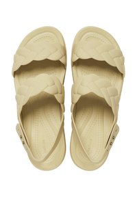 Beiga sandaler med flätade remmar, tillverkade av mjukt material. Har justerbar sidspänne och texturerad fotbädd för komfort.