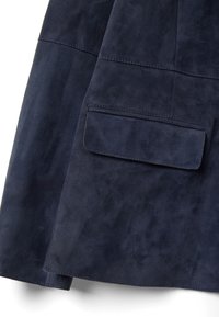 Chaqueta de ante azul marino con una textura suave, que presenta una costura horizontal y un bolsillo con solapa en la parte inferior izquierda.