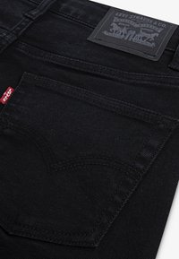 Black denim jeans with a structured design, featuring a prominent back pocket and a leather patch with brand logo. Smooth texture and neat stitching.