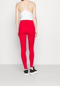 Röda leggings med hög midja och vita sidremsor, kombinerat med en vit ärmlös topp. Tyget ser slätt och åtsittande ut.