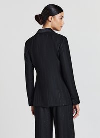 Blazer noir �à rayures verticales avec un col en satin, mettant en valeur des rayures verticales et des accents scintillants. Coupe ajustée avec des détails de poignets à boutons.