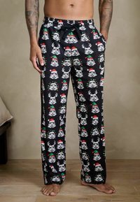 Fekete pizsananadrág, amelyet ismétlődő minták díszítenek: stormtrooper sisakok, amelyek Mikulás sapkát és agancsot viselnek, puha anyagból készült, oldalzsebekkel.