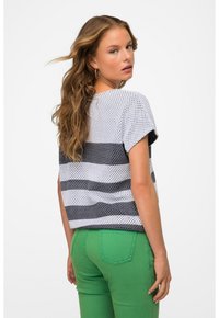 Top de manga corta en tejido ligero y transpirable con un patrón de rayas en blanco y gris oscuro; combinado con pantalones ajustados verdes.