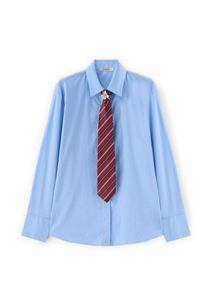 Světle modrá košile s dlouhým rukávem a špičatým límečkem, doplněná červenou pruhovanou kravatou a malou květinovou broží u límce.