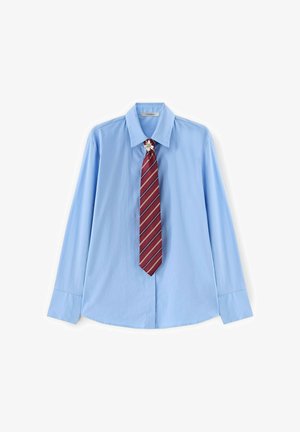 Světle modrá košile s dlouhým rukávem a špičatým límečkem, doplněná červenou pruhovanou kravatou a malou květinovou broží u límce.