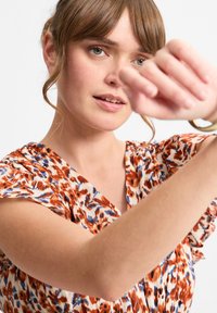 Blumendruckkleid in Creme-, Orange- und Blautönen. Mit V-Ausschnitt und kurzen Rüschenärmeln. Glattes Gewebe mit leichter Textur.