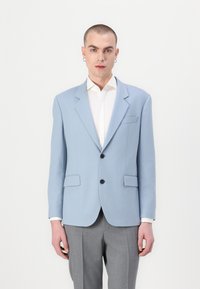 Blazer azul claro con solapas de muesca, dos bolsillos frontales y botones negros, combinado con una camisa blanca y pantalones grises. Textura de tela suave.