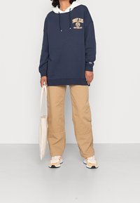 Námořnický oversized mikina s bílou vrstvenou kapucí, zdobená tištěným logem. V kombinaci s béžovými cargo kalhotami a vícebarevnými teniskami.