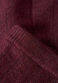 Bordowy dzianinowy materiał o żebrowej strukturze, prezentujący miękką, lekko puszystą powierzchnię oraz wzór w diamenty; ciepłe i przytulne wrażenie.