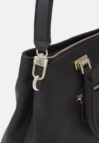 Sangle de sac à main en cuir noir texturé, attachée avec un fermoir en métal argenté, et une fermeture éclair visible le long du bord supérieur.