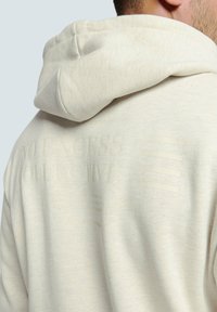 Crème kleurige hoodie met een gestructureerde, reliëf merknaam en strepen op de achterkant. Gemaakt van zachte stof met een ontspannen pasvorm.