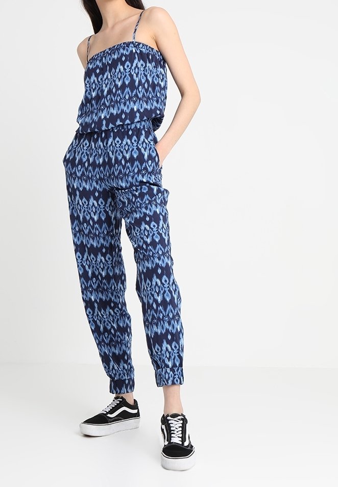 Dwuczęściowy kombinezon w granatowym i niebieskim kolorze, z wzorzystym topem na ramiączkach i zwężanymi spodniami z elastycznym pasem.