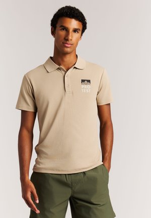 Beige poloshirt van gestructureerde stof, met drieknoopssluiting, korte mouwen en een zwart logo op de borst. Gecombineerd met groene shorts.