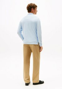 Jasnoniebieska koszula polo z długim rękawem i kołnierzykiem, połączona z jasnobeżowymi spodniami i czarnymi butami, widziana z tyłu.