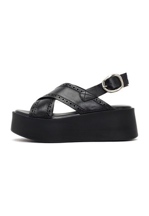 Sandalia de plataforma negra con suela gruesa, tiras de cuero cruzadas, pequeños detalles perforados y correa ajustable con hebilla plateada alrededor del talón.