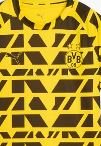 Camiseta de fútbol amarilla y negra del Borussia Dortmund con un patrón geométrico, logo de Puma en el lado izquierdo del pecho y escudo del club BVB 09 en el lado derecho del pecho.
