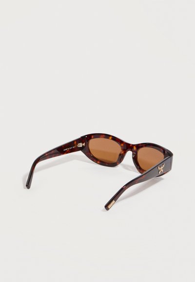 Γυαλιά ηλίου με σχέδιο από χελώνα, φακούς καφέ και ένα μικρό χρυσό έμβλημα μέλισσας στα πλευρικά πλαίσια.