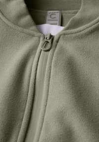 Veste en polaire verte zippée avec une surface texturée, un col montant et un détail de tirette contrastant. Étiquette visible à l'intérieur du col.