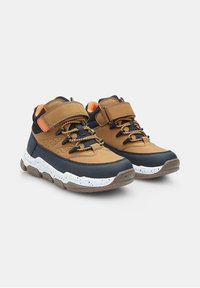 Zapatillas altas marrones y azul marino con parte superior texturizada, acentos naranjas en contraste y una suela blanca moteada. Cuenta con una correa de velcro.