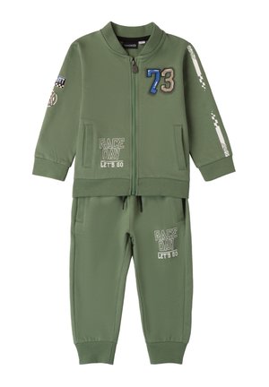 Completo tuta verde realizzato in tessuto morbido, con giacca a zip decorata da toppe e pantaloni della tuta abbinati con grafiche stampate.