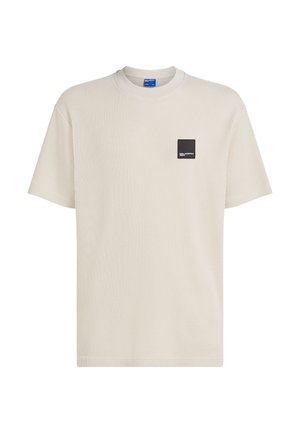 Gaiši bēša ribaina T-krekla ar apaļu kaklu un īsām piedurknēm. Kreisajā krūtīs ir melna kvadrātveida uzlīme ar baltu tekstu.