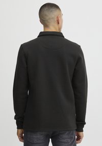 Svart sweatshirt med lange ermer, krage og en jevn tekstur. Har en avslappet passform og minimalistisk design, med sømdetaljer bak.