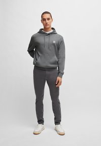 Grå hoodie med framficka och logotypplåster, tillsammans med grå slim-fit byxor och vita sneakers. Slätt tyg med avslappnad passform.