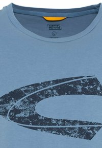 Helle blaue Baumwoll-T-Shirt mit Rundhalsausschnitt. Verfügt über ein dunkelblaues, verwittertes Grafikdesign. Das Etikett trägt die Aufschrift "camel active", Größe L.