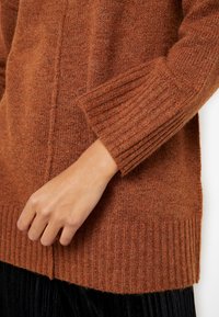 Maglione marrone lavorato a maglia con polsini e orlo a costine, caratterizzato da una texture morbida e una leggera variazione di colore, che mette in risalto un design aderente.