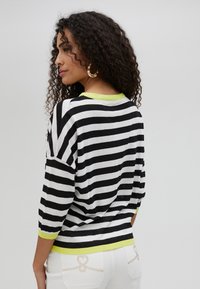 Black and white striped sweater with a loose fit, featuring a lime green ribbed neckline and cuffs. Soft texture, three-quarter sleeves, and drop shoulders.
